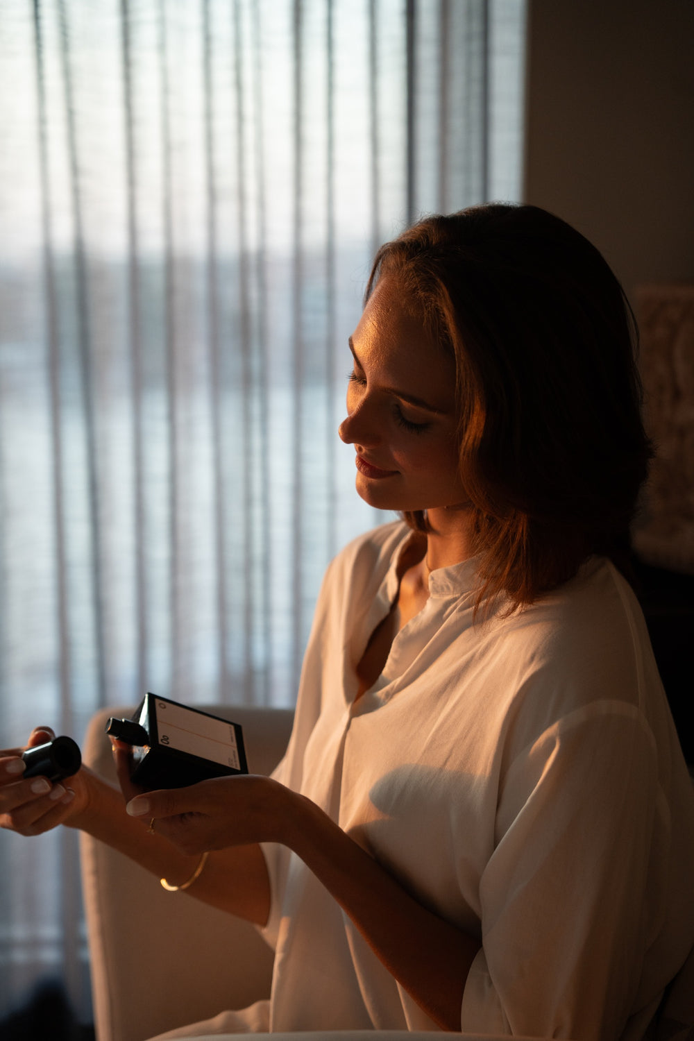 A woman in warm window light holding perfume 852 Serenity